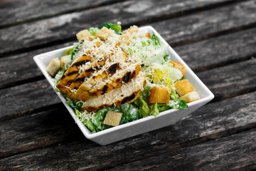 Caesar salad with chicken and lettuce on wooden table