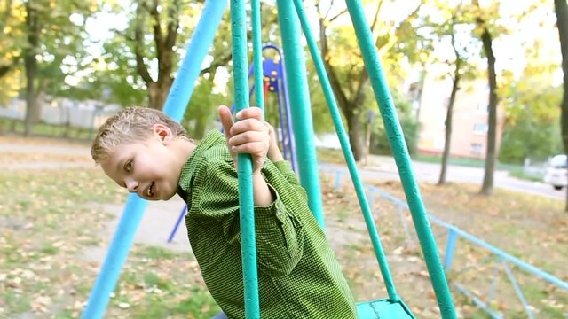 Cute child on swing. Little boy rides on swing on children playground. Slow motion portrait of funny face of little 8 years old kid playing outside on autumn warm sunny day.