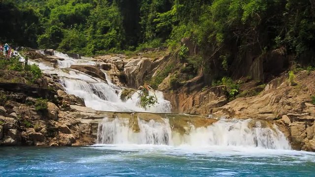 waterfall flows among rocks falls into lake in tropical park