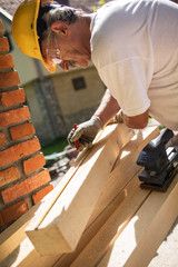 Senior man finishing wooden beam with sander