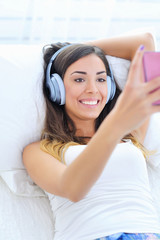 Beautiful young woman in headphones listening to music from her mobile phone in bed