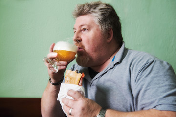 Uomo robusto che mangia un panino e beve birra al bar