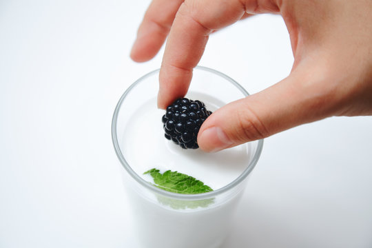 Hand puts blackberry in glass of milk