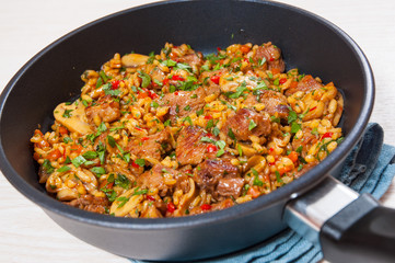 Rice with meat, vegetables and mushrooms in a frying pan