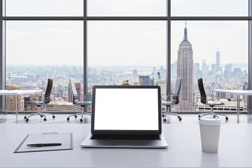 A workplace in a modern panoramic office in Manhattan, New York. A laptop with white screen, notepad and a coffee cup are on the white table. Black Leather chairs. Open space. 3D rendering.
