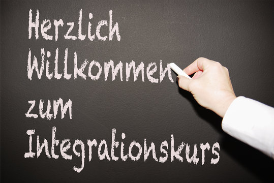 Lehrerin scheibt an die Tafel "Herzlich willkommen zum Integrationskurs"
