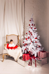  little girl sits in a chair near the Christmas tree