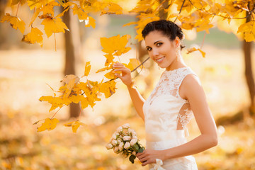 Happy bride in autumn park. Smiling girl in a white dress, outdoors