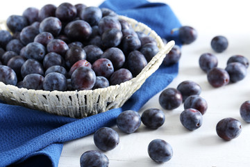 Fresh plums in basket on the white wooden background