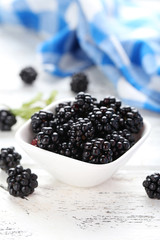 Beautiful ripe blackberry in bowl on white wooden background