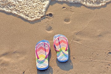 Fototapeta na wymiar flip-flops and footprints in beach sand with surf