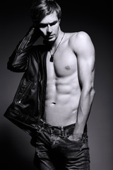 Young handsome muscled fit male model man in leather jacket posing in studio showing his abdominal...