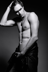Obraz premium Young handsome muscled fit male model man in leather jacket posing in studio showing his abdominal muscles