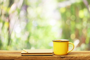 Notebook  and coffee in yellow cup on wooden table