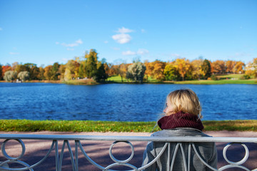 Fototapeta premium girl sitting on a bench by the lake in the autumn park