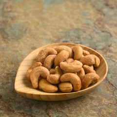 Salted cashew nuts or seeds on small bamboo plate, photographed on slate with natural light (Selective Focus, Focus on the cashews in the front)