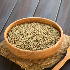 Raw lentils (lat. Lens culinaris) in wooden bowl, photographed on dark wood with natural light (Selective Focus, Focus one third into the raw lentils)