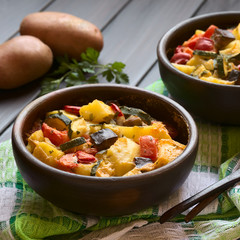 Baked potato, eggplant, zucchini and tomato casserole in rustic bowl, photographed with natural light (Selective Focus, Focus in the middle of the dish)