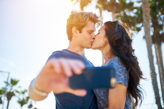couple kissing for romantic selfie in front of sun and palm trees