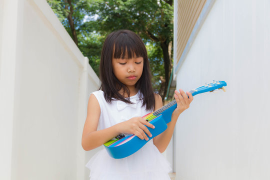 Young asian funny girl having fun and playing on small colorful ukulele guitar