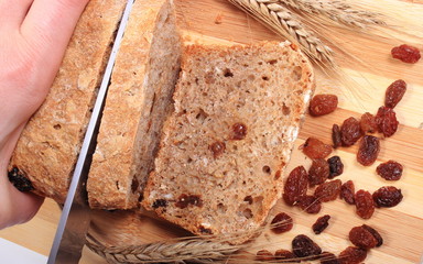 Slicing fresh bread, ears of wheat and raisins