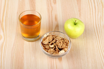 Apple juice in a glass and the cereal in the bowl and Apple on wooden background
