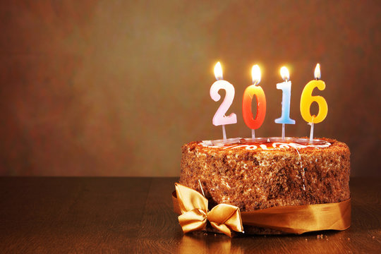 New Year 2016 still life. Chocolate cake and burning candles on brown background