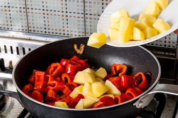 Versamento di pezzi di patate nella pentola con rondelle di peperoni rossi 