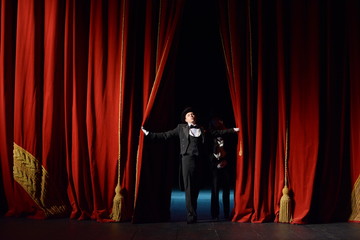 the actor in a tuxedo and hat opens the stage curtain