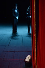 the actor in a tuxedo and hat with a mask opens the stage curtain