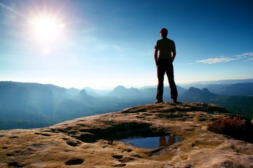 Obraz premium Alone man in red cap on peak of sharp peak in rock empires park and watching over the misty and foggy morning valley to Sun. Beautiful moment