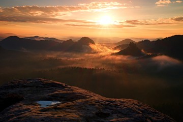 View over wet sandstone cliff into  heavy misty valley in Saxony Switzerland. Peaks of hills increased fromdense  fog