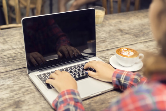 Hipster girl hands, laptop and coffee mug on a wooden table