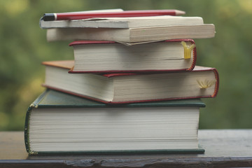pile of old books, note pad and pencil on a garden wooden table