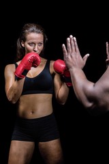 Female boxer with fighting stance against trainer hand