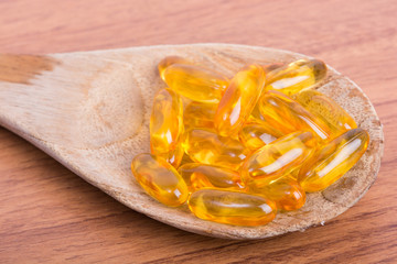 Cod liver oil omega 3 gel capsules on spoon wood