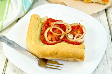 Pie with onions and tomatoes in white plate on board