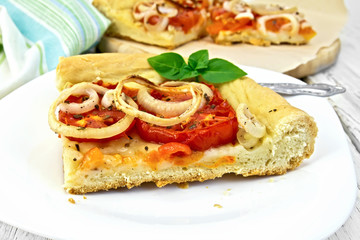 Pie with onions and tomatoes in white plate on light board