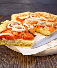 Pie with onions and tomatoes on paper with knife