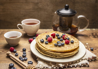 delicious breakfast with pancakes with honey,honey spoon and berries with a cup of tea on wooden background close up