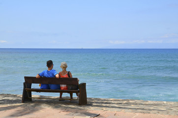 Young couple sitting on a bench by the ocean.