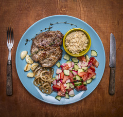fried pork with salad on a plate with knife and fork on rustic wooden background top view