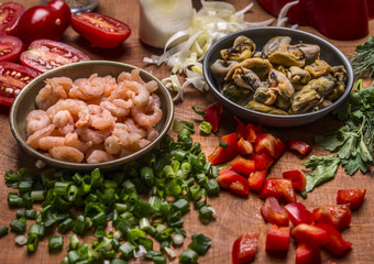 peeled shrimp and mussels with chopped pepper and green onions tomatoes on a wooden background close up