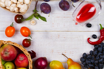 Mushrooms, grape, plums, onion, tomatoes, chilli peppers, glass of red wine, apples and pears in basket. View from above; top studio shot