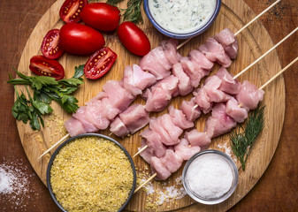 Fresh raw sliced turkey breast on skewer  with bulgur, with tomato sauce and herbs with salt on a cutting board on a wooden background top view close up