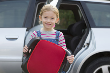 Portrait Of Girl Holding Booster Seat Standing Next To Car
