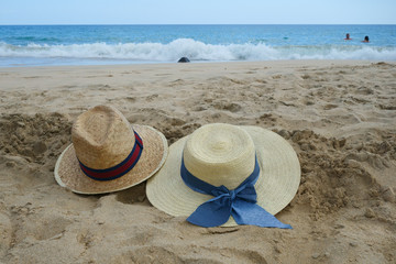 Couples straw sunhats in the sand on a sunny beach whilst owners swim in sea.