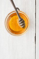 Honey in the glass bowl with dipper on the white wooden table