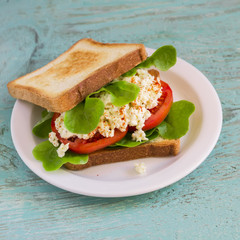 sandwich with egg, tomato and lettuce on a white plate on blue wooden surface