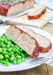 Homemade meatloaf garnished with green peas on a white plate